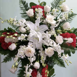 White lilies and roses arranged with red carnations on a standing cross