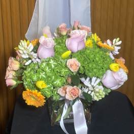 Pink roses and yellow-orange flowers in a glass vase with a white ribbon