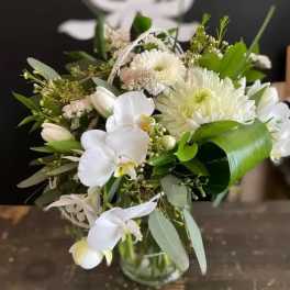 White floral bouquet in a glass vase with orchids and daisies