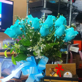 Blue roses in a glass vase with a ribbon and chocolates in a gift bag