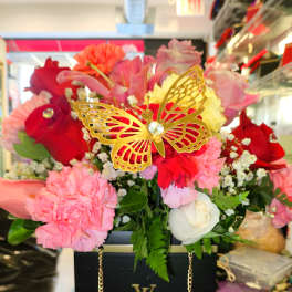 Mixed pink and red flower arrangement in a black box with a gold butterfly