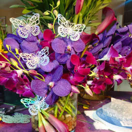 Purple orchids and pink calla lilies in a glass vase with butterfly picks