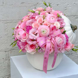 Pink floral arrangement in a white pumpkin-shaped vase with a ribbon bow