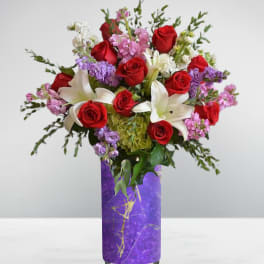 Bouquet of red roses, white lilies, and pink flowers in a purple vase