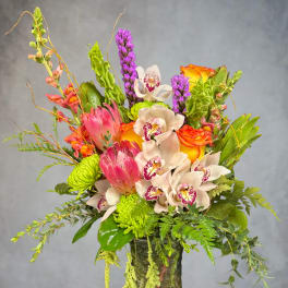 Mixed bouquet with orchids, roses, and green blooms in a glass vase