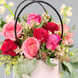 Pink and red roses arranged in a white basket with black handles