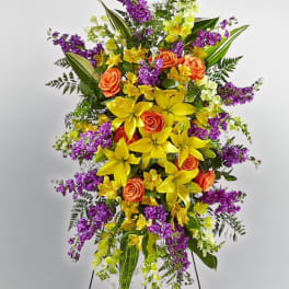 Tall floral standing spray with yellow lilies, orange roses, and purple blooms