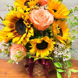 Basket arrangement of sunflowers and peach roses with small white filler flowers
