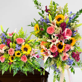 Colorful sunflower, lily, and rose sympathy sprays on a wooden casket and standing easel