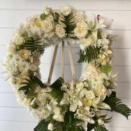 White floral wreath on a wooden easel with roses and lilies