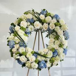Large floral wreath on a wooden easel with white, blue, and green blooms