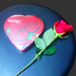 Single red rose beside a heart-shaped Valentine candy box
