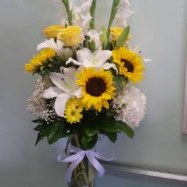 Tall bouquet of sunflowers, white lilies, and yellow roses in a glass vase