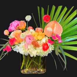 Colorful mixed bouquet in a clear glass vase with palm fronds