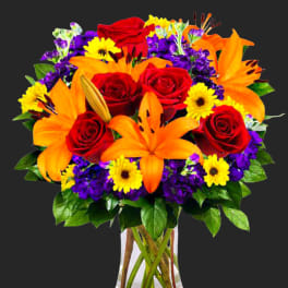 Bouquet of red roses, orange lilies, and yellow daisies in a clear vase