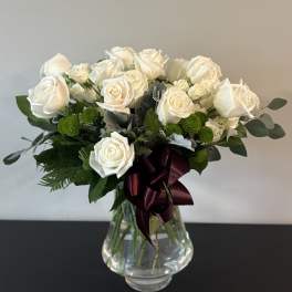 White rose bouquet in a clear glass vase with a burgundy ribbon