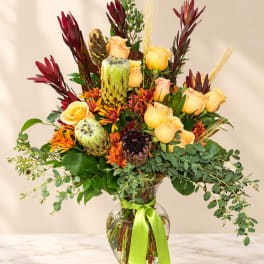 Mixed bouquet of yellow roses and orange flowers in a glass vase with a green ribbon