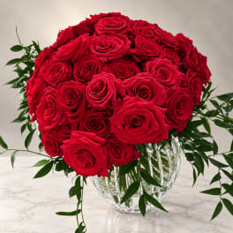 Red rose bouquet in a clear glass vase with trailing greenery