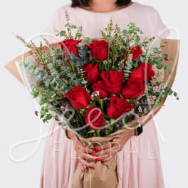 Hand-tied bouquet of red roses with eucalyptus accents wrapped in kraft paper.
