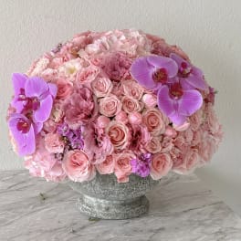 Pink rose and orchid arrangement in a stone pedestal vase