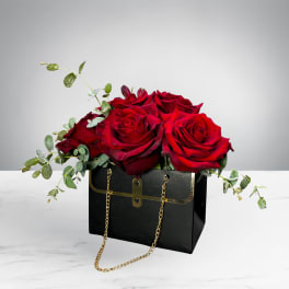 Red roses arranged in a black handbag-style box with gold chain handles