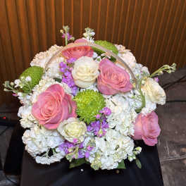 Basket arrangement of pink and white roses with white hydrangeas and green mums