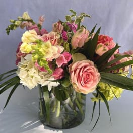 Pastel pink and yellow arrangement with roses, snapdragons, and hydrangeas in a clear glass vase