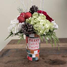 Holiday floral arrangement in a patterned vase with red ornaments and pinecones