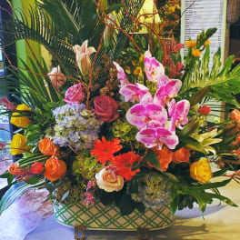Large colorful arrangement of orchids, roses, hydrangeas, lilies, and gerberas in a patterned ceramic container