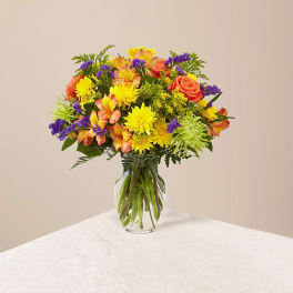 Mixed bouquet of yellow, orange, and purple flowers in a clear glass vase