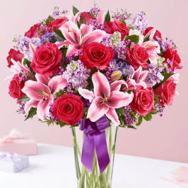 Bouquet of red roses and pink lilies in a clear glass vase with a purple ribbon