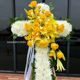 Yellow roses and lilies with white chrysanthemums on a standing cross arrangement