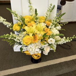 Yellow and white floral arrangement in a black vase with a yellow ribbon