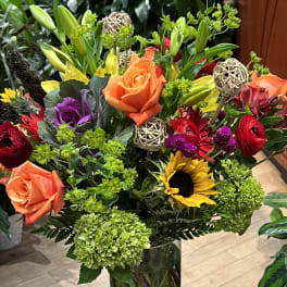 Mixed bouquet with roses, lilies, sunflowers, and hydrangeas in a glass vase