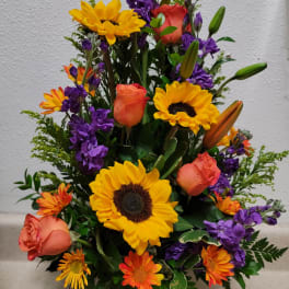 Mixed bouquet of sunflowers, orange roses, and purple flowers in a glass vase