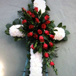 Cross-shaped floral tribute with red roses and white flowers on a stand