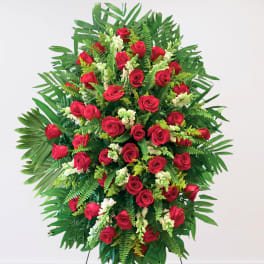 Standing spray of red roses with white accents and tropical greenery