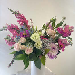 Mixed pink and lavender flowers arranged in a tall white vase
