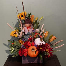 Fall floral arrangement with pumpkins, roses, sunflowers, and a scarecrow