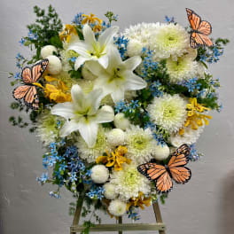 Heart-shaped floral arrangement with white lilies, chrysanthemums, blue flowers, and butterfly accents