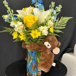 Bouquet of yellow and white flowers in a glass vase with a teddy bear
