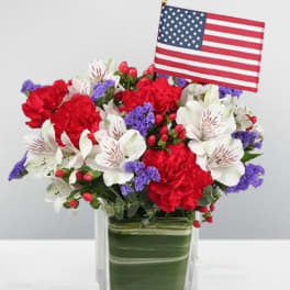 Red, white, and purple floral arrangement in a glass vase with an American flag