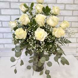 Tall arrangement of white roses and baby's breath in a clear glass vase with cascading eucalyptus