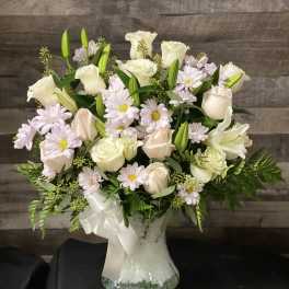 White roses and pale daisies arranged in a glass vase with a ribbon