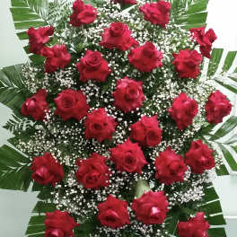 Standing spray of red roses with white filler and large tropical leaves