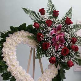 Heart-shaped floral wreath with red roses and white flowers on an easel