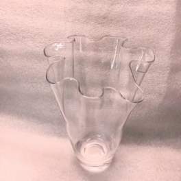 Clear glass vase with a wavy flared rim on a soft pink background