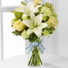 White lilies and pale yellow roses in a clear glass vase with a striped ribbon.