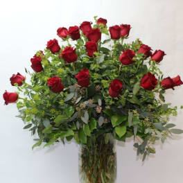 Red roses arranged in a tall glass vase with greenery