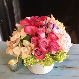 Pink roses and orchids arranged in a white vase with a small candle beside it.
